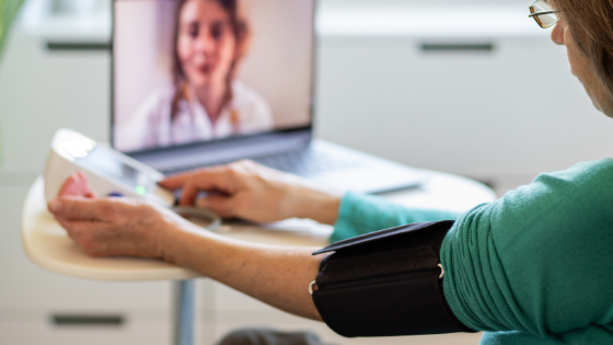 An older adult using a tablet for a telehealth video visit with support from a community helper